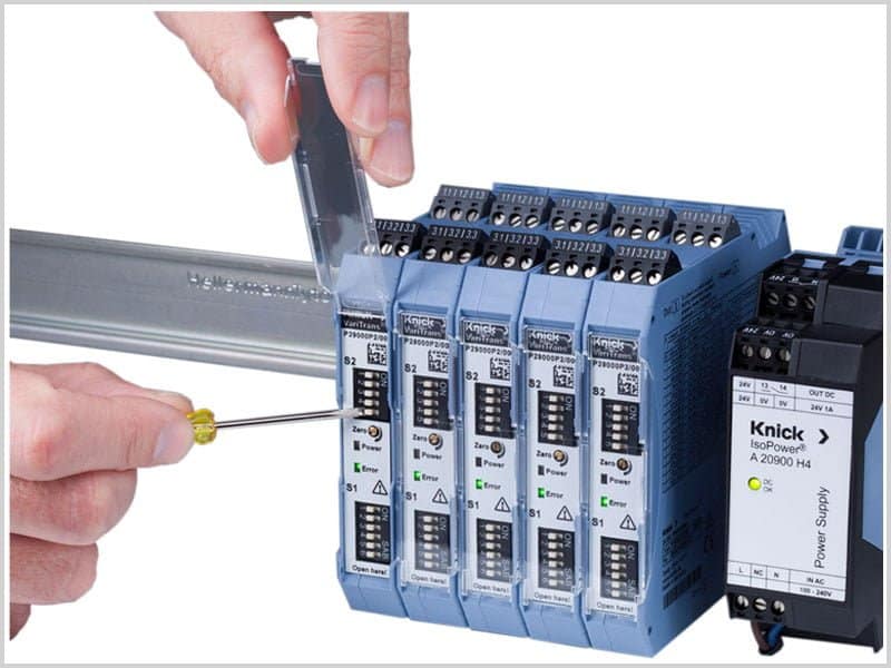 the knick 29000 mounted on a din rail. a hand lifting the protective cover, the other adjusting the dip switches with a small screwdriver